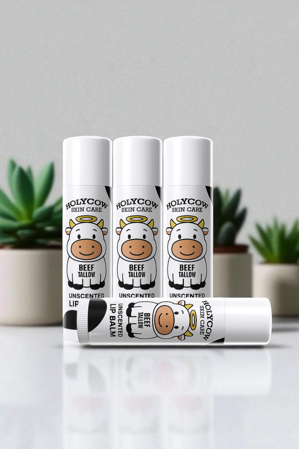 Three lip balm containers with cow design on a white surface and gray background